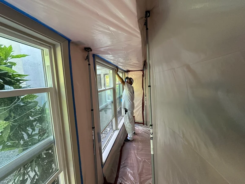 Worker in protective suit painting interior walls with spray equipment