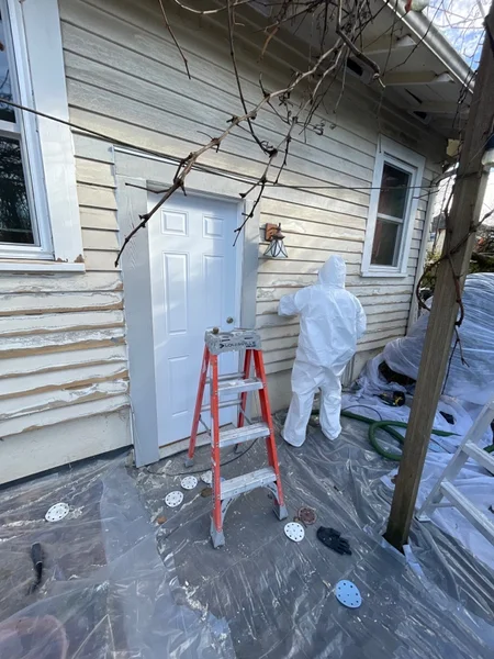 Worker in protective suit cleaning exterior siding near entrance