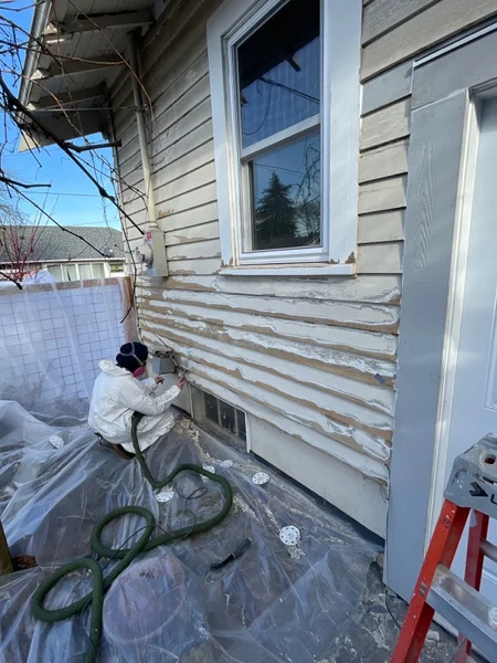 Worker in protective suit removing old siding from house exterior