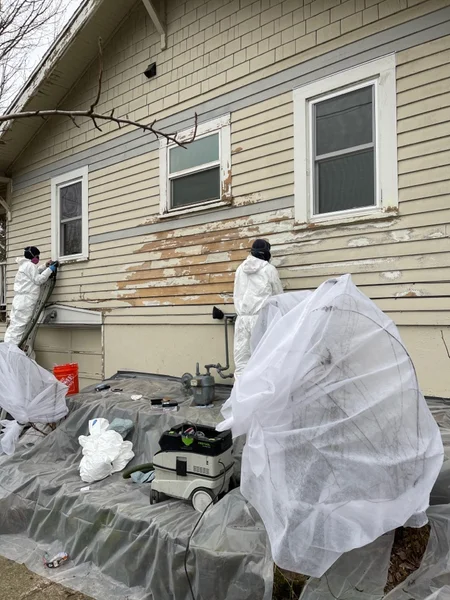 Workers in protective suits removing lead paint from house siding