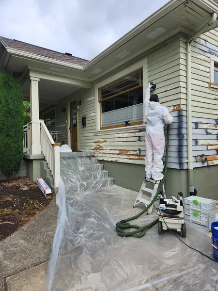 Worker in protective suit removing old siding from house exterior with plastic sheeting covering area