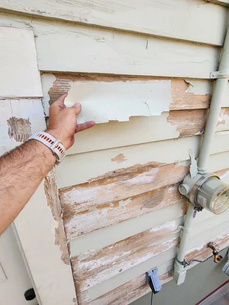 During: hand removing peeling white paint from wood siding