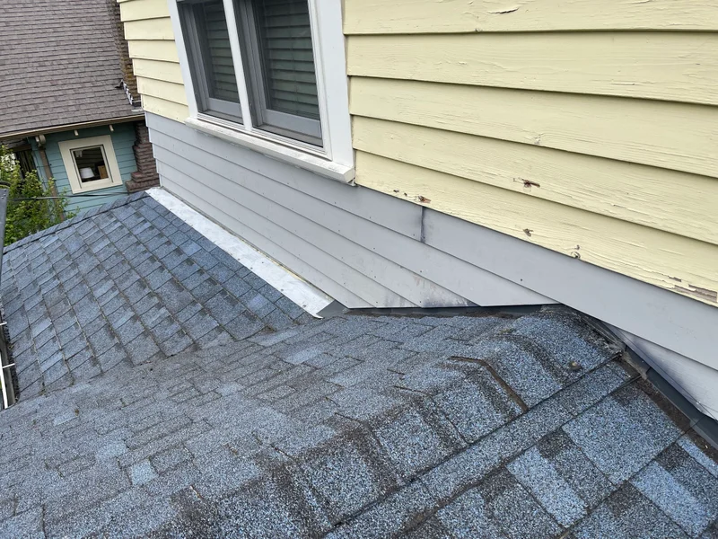 Damaged roof section with water damage and deteriorating shingles near house siding