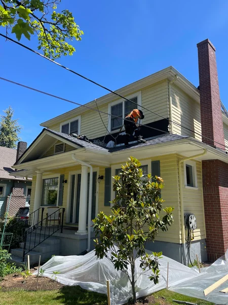 Worker performing roof repair on yellow two-story house with brick chimney