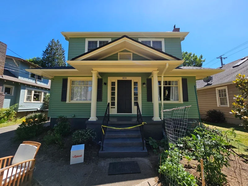 Exterior view of a green craftsman-style house with front porch and landscaping