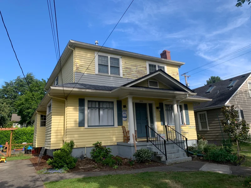 Yellow two-story house with front porch and steps in residential neighborhood